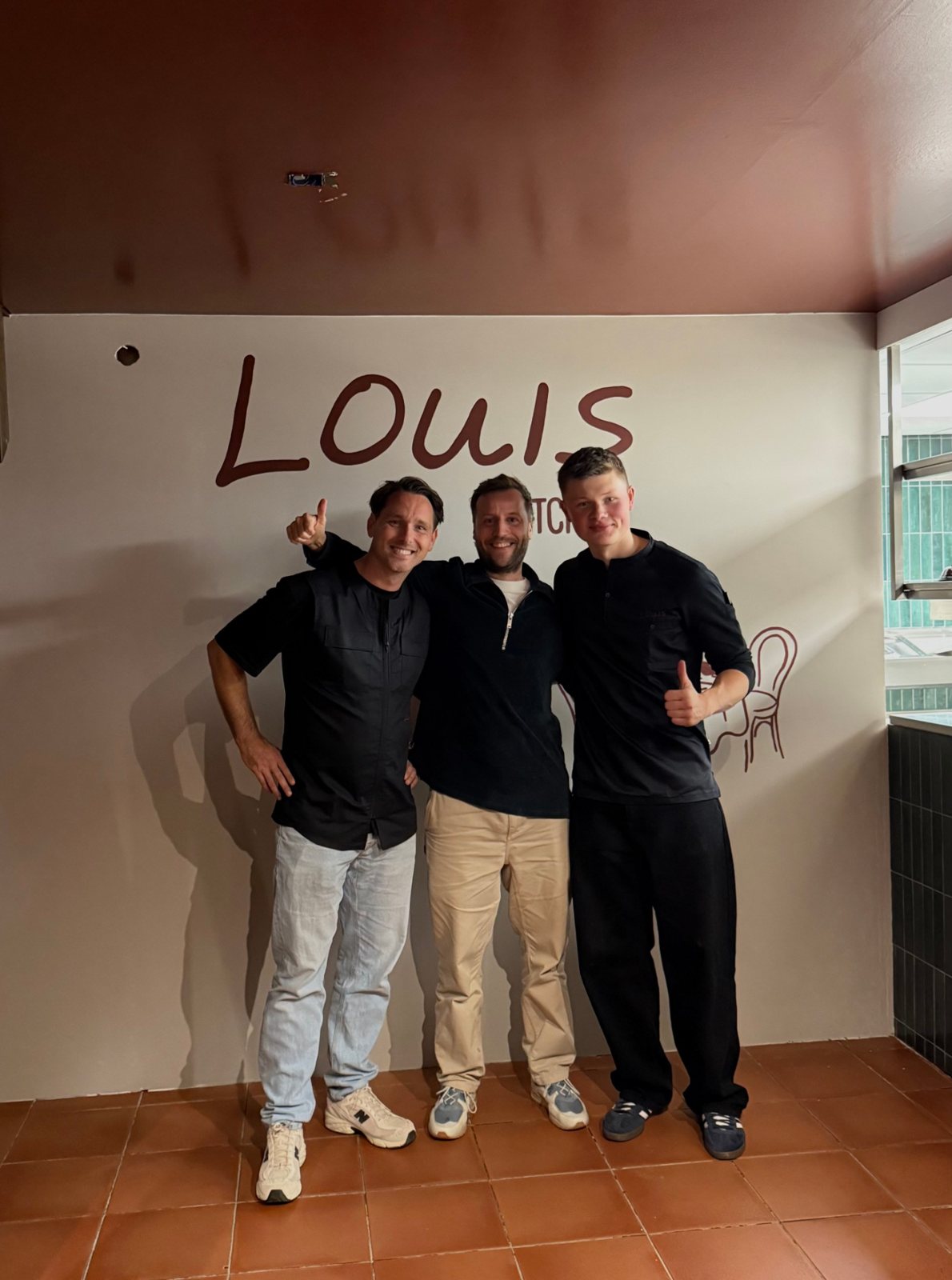 Three men giving a thumbs up in front of the wall with the Louis logo in the new restaurant in Groningen